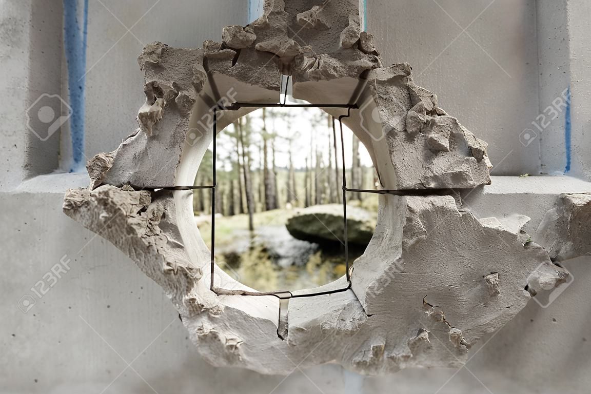 In a concrete fence a hole overlooking the pine forest