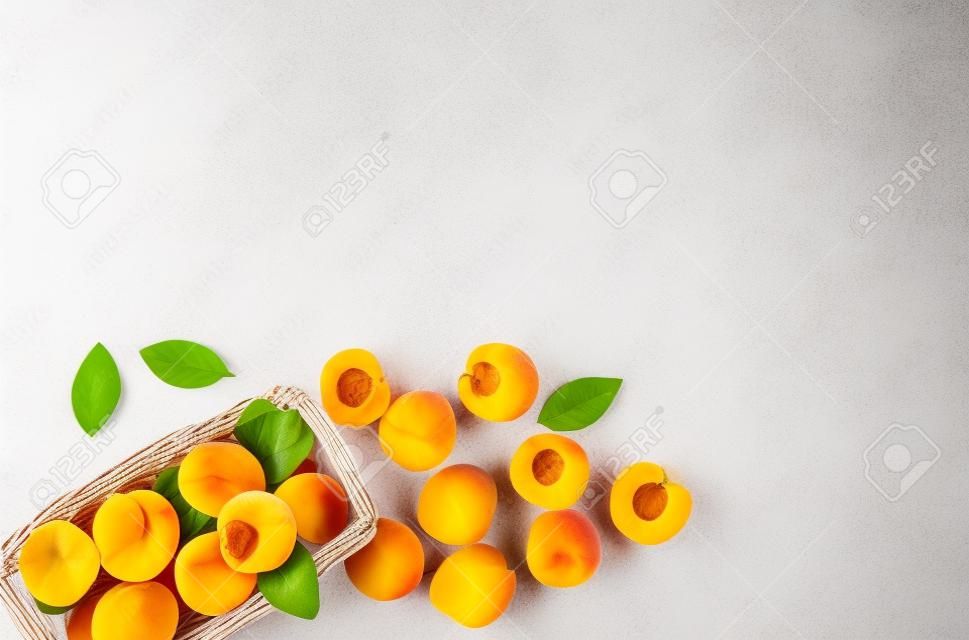 Fresh raw apricots in basket on white background top view copy space, pattern with leaves