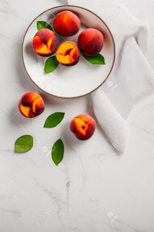 Summer lunch. Red peaches on white background with tablecloth and leaves top-down.