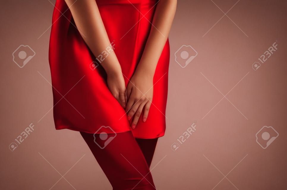 Woman in a red dress holding hands between legs. Experiencing pain, discomfort. Women's health, gynecology.