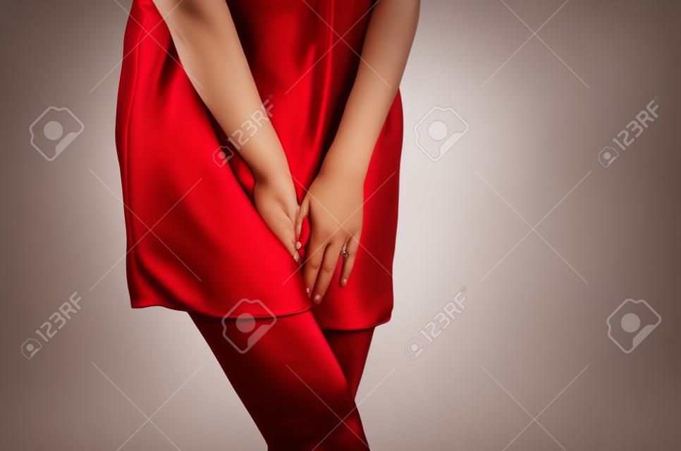 Woman in a red dress holding hands between legs. Experiencing pain, discomfort. Women's health, gynecology.