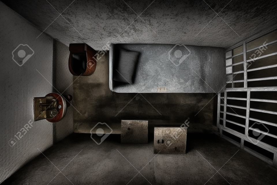 Top Blick auf alte Gefängniszelle gesperrt für eine Person mit Bett, Waschbecken, Toilette und Stuhl. Düstere Atmosphäre.