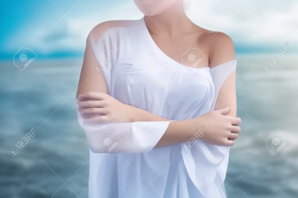 Atraente jovem fêmea em enquanto blusa e calcinha abraçando-se e mantendo os olhos fechados enquanto está perto de água no dia ventoso