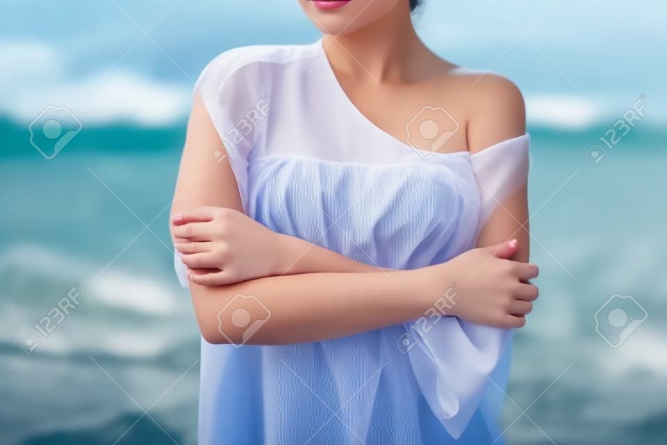 Atraente jovem fêmea em enquanto blusa e calcinha abraçando-se e mantendo os olhos fechados enquanto está perto de água no dia ventoso