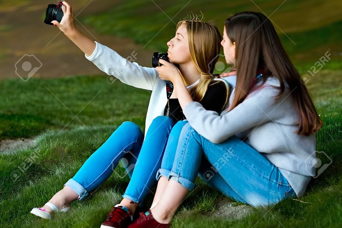 两个十几岁的女孩。夏天自然。他们放学后坐在草地上。换个地方做萨尔菲。他在社交网络中为自己拍照。
