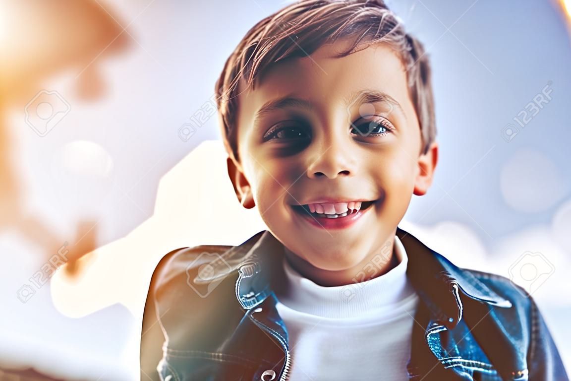 Mały chłopiec cute uśmiecha się i spojrzenie na aparat fotograficzny podczas zabawy na świeżym powietrzu.