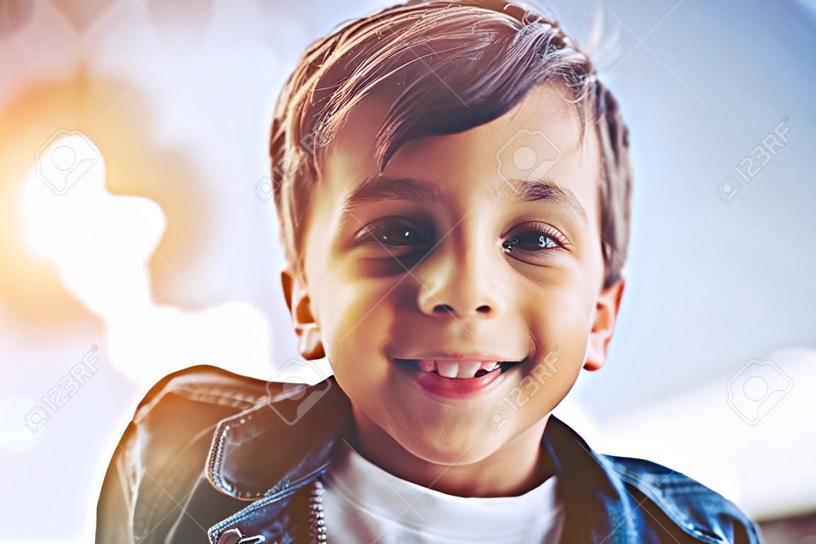 小さなかわいい男の子は、屋外で楽しみながら、笑顔でカメラを見ています。