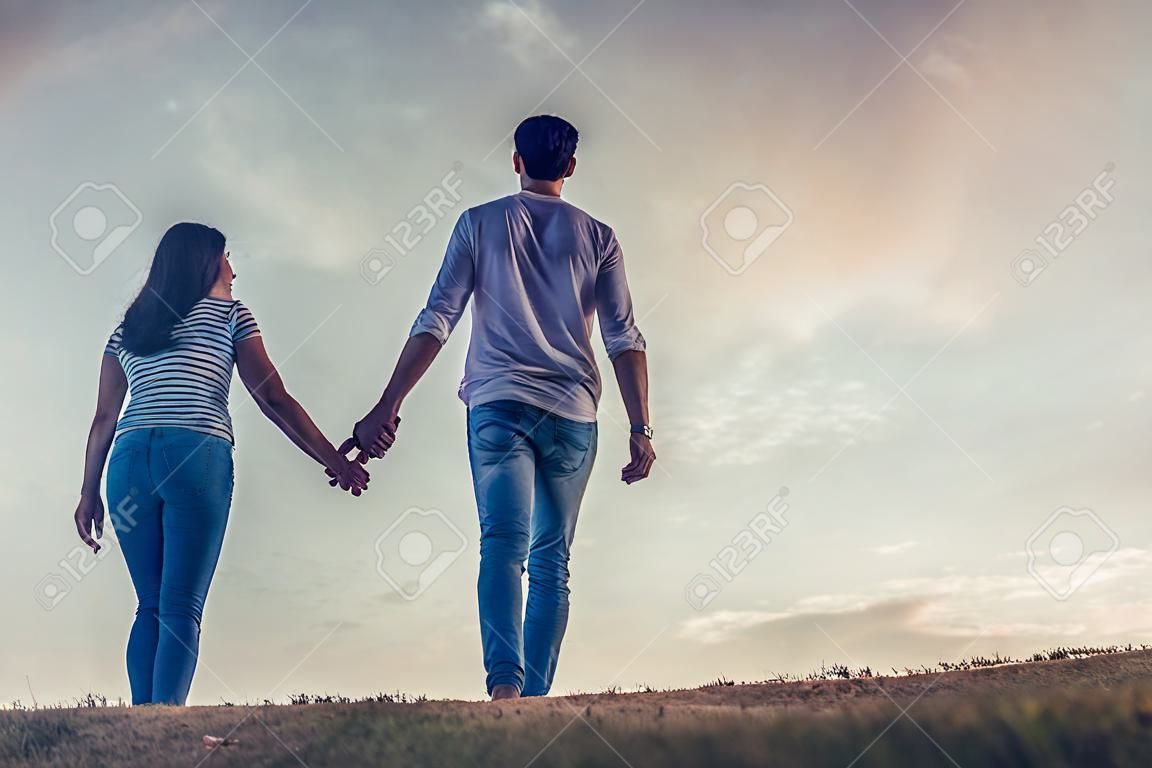 Bild in voller Länge von den schönen romantischen Paaren, welche draußen die Firma von einander genießen und Hände auf dem Hintergrund des Himmels halten.