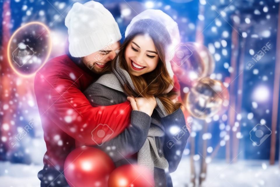 若いロマンチックなカップルは、クリスマスの前に冬に屋外で楽しんでいます。大晦日に一緒に過ごす時間を楽しんでいます。二人の恋人が聖バレンタインデーに抱き合ってキスをしています。