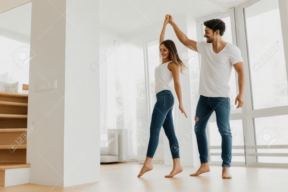 Romantic couple at home. Attractive young woman and handsome man are enjoying spending time together. Passionate couple is dancing on light modern kitchen with paniramic windows.