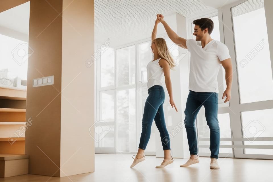 Romantisch stel thuis. Aantrekkelijke jonge vrouw en knappe man genieten van tijd samen doorbrengen. Gepassioneerd stel danst op lichte moderne keuken met paniramische ramen.