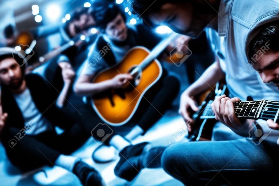 Repetition of rock music band. Guitar players and drummer are sitting on the floor at rehearsal base.