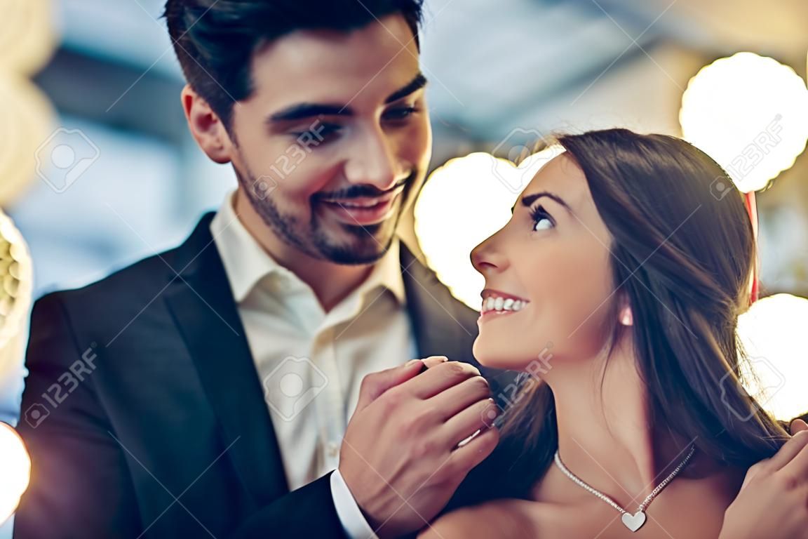 美しい愛情のあるカップルは、モダンなレストランで一緒に時間を過ごしています。ドレスとスーツのハンサムな男性の魅力的な若い女性は、ロマンチックなディナーを持っています。聖バレンタインデーを祝う。