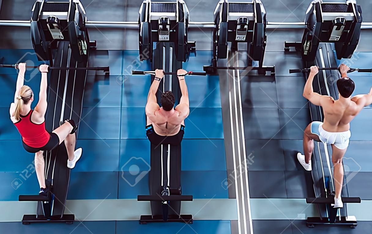 Group of sporty muscular people are working out in gym. Cross fit training. Paddling training apparatus. Top view of four sportsmen are rowing together.
