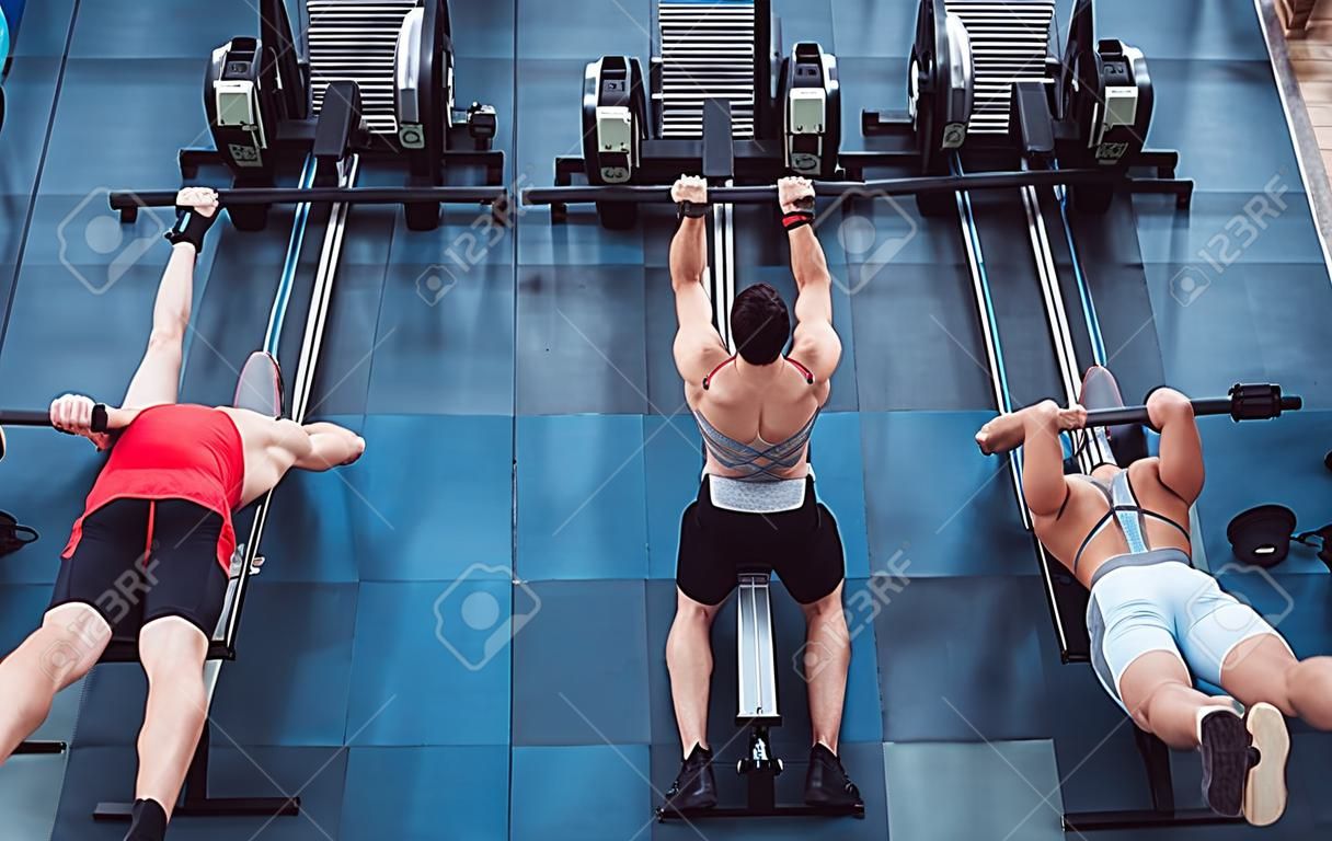 Group of sporty muscular people are working out in gym. Cross fit training. Paddling training apparatus. Top view of four sportsmen are rowing together.