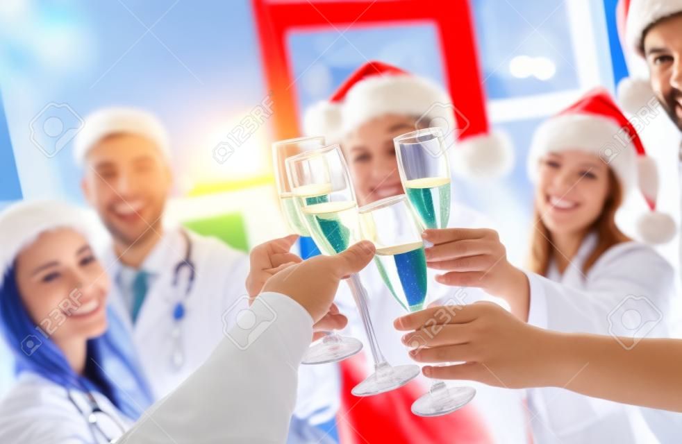 Joyeux Noel et bonne année! Groupe de médecins célébrant les vacances d'hiver au travail. Personnel médical en uniforme et chapeaux de Père Noël buvant du champagne ensemble.