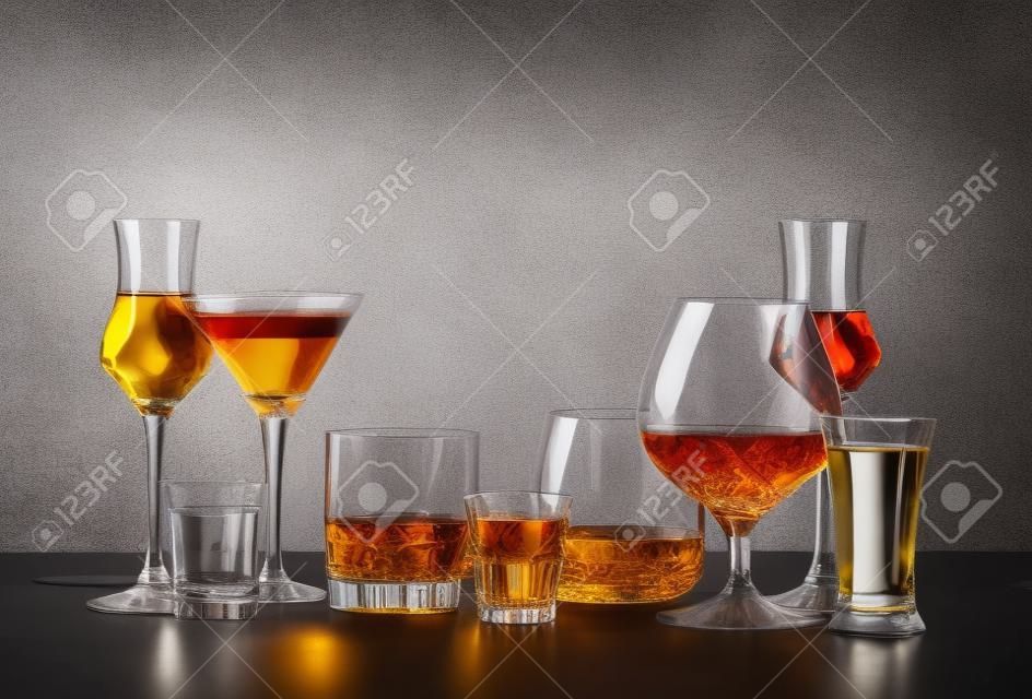 Set of strong alcoholic drinks in glasses in assortment: vodka, cognac, tequila, brandy and whiskey, grappa, liqueur, vermouth, tincture, rum. Gray bar counter background, copy space, toned