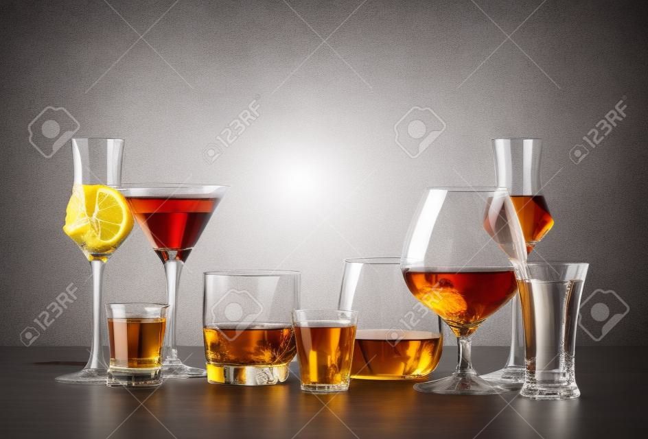 Set of strong alcoholic drinks in glasses in assortment: vodka, cognac, tequila, brandy and whiskey, grappa, liqueur, vermouth, tincture, rum. Gray bar counter background, copy space, toned