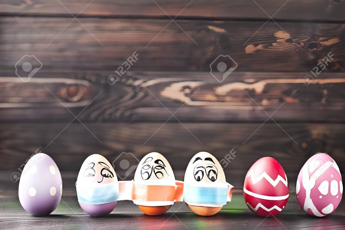 Row colorful easter eggs painted and in medical mask with funny faces on dark wooden background