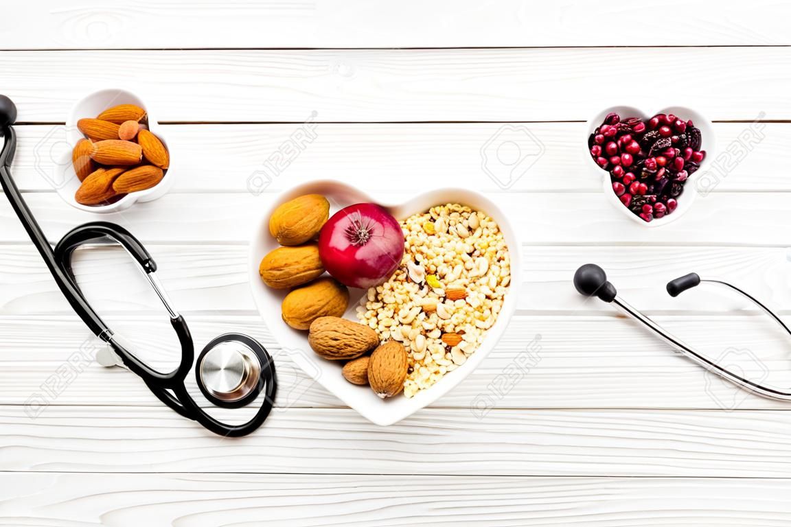 Groenten, fruit, noten in hartvormige kom in de buurt stethoscoop op wit houten achtergrond top uitzicht