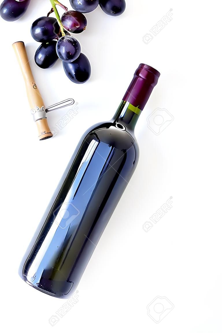 Concepto de vino tinto. Botella de vidrio con bebida cerca de racimo de uvas y sacacorchos en la vista superior de fondo blanco.