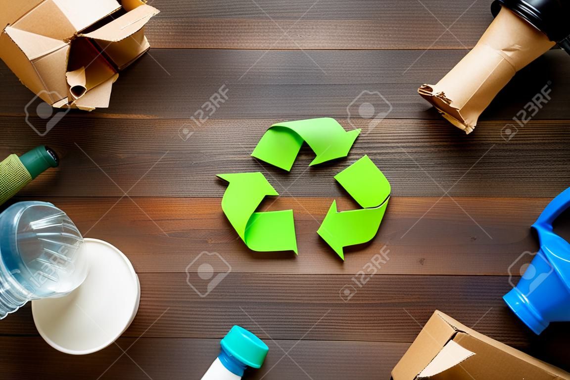 Raccolta differenziata. Simbolo ecologico di riciclo verde. Le frecce riciclate firmano vicino a materiali per il riciclo e il riutilizzo su sfondo di legno scuro vista dall'alto