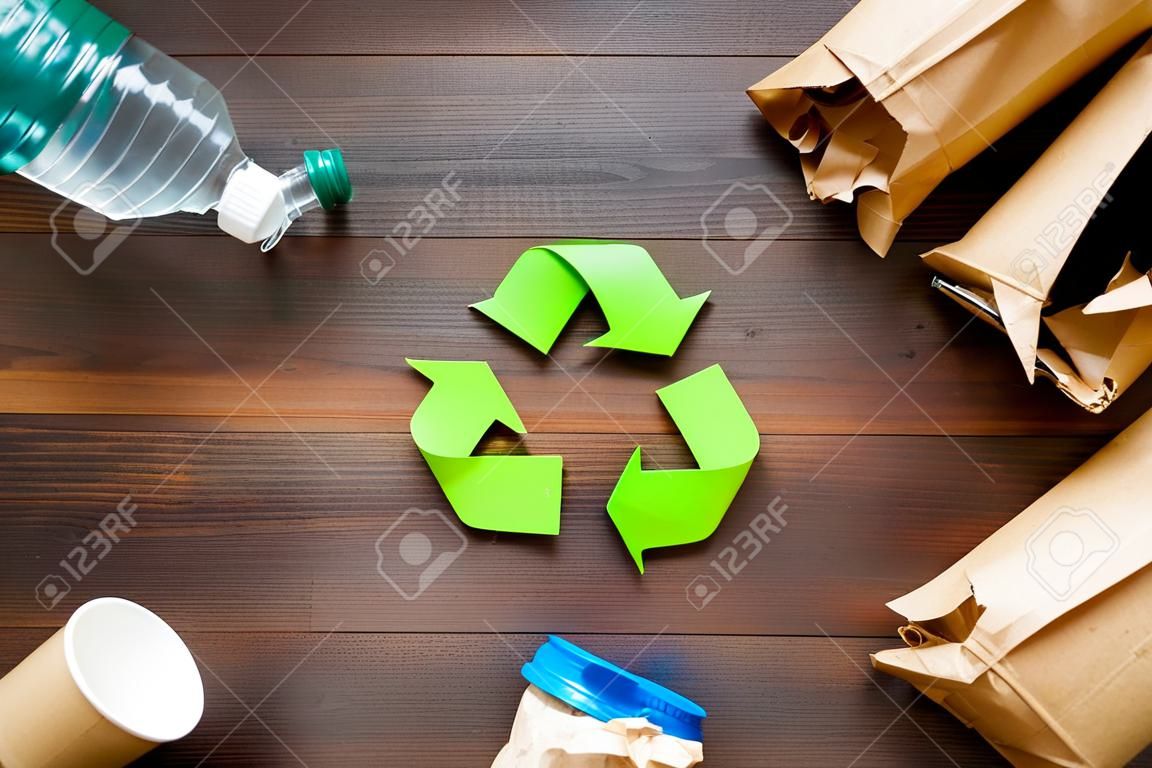 Raccolta differenziata. Simbolo ecologico di riciclo verde. Le frecce riciclate firmano vicino a materiali per il riciclo e il riutilizzo su sfondo di legno scuro vista dall'alto