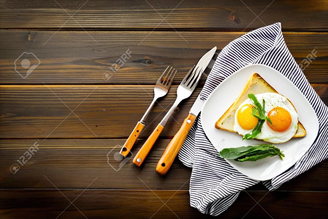 Recipe of fried eggs for vegetarian breakfast. Fried eggs with cherry tomatoes and greenery near toast with avocado on dark wooden background top view copy space