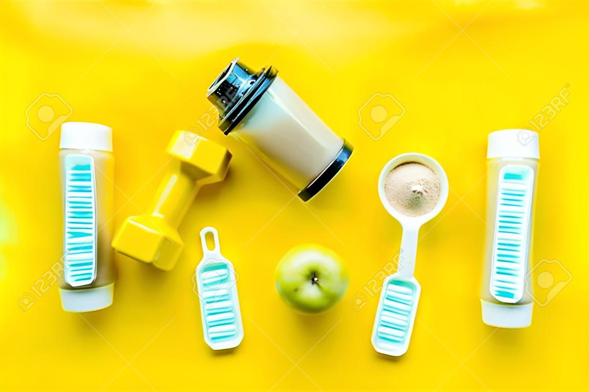 sport nutrition set with protein powder for cocktail and scoop on yellow background top view space for text