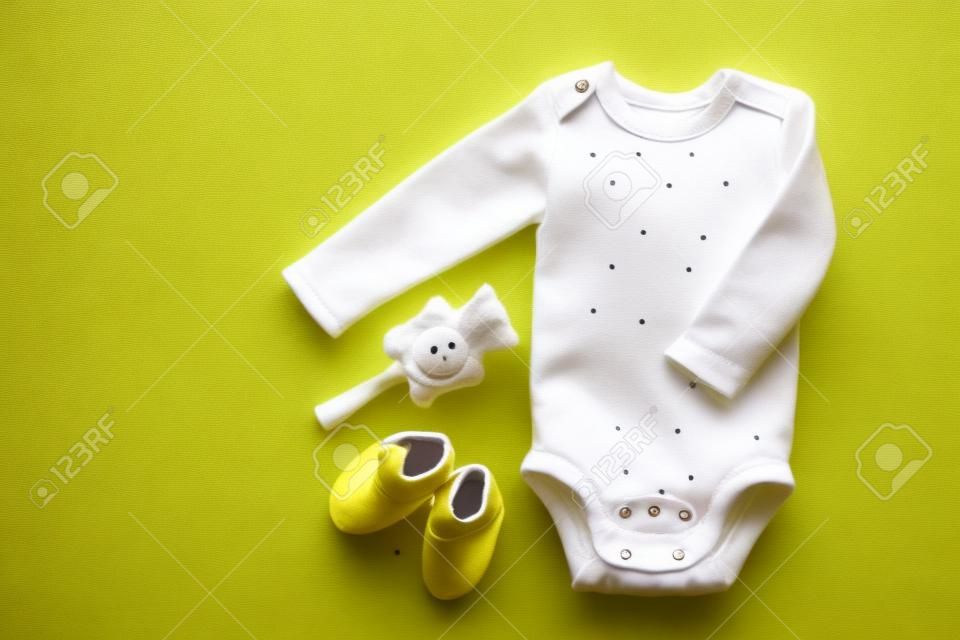 Linda ropa de bebé - traje - botines y accesorios en la mesa amarilla de arriba hacia abajo.