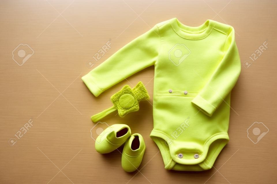 Linda ropa de bebé - traje - botines y accesorios en la mesa amarilla de arriba hacia abajo.