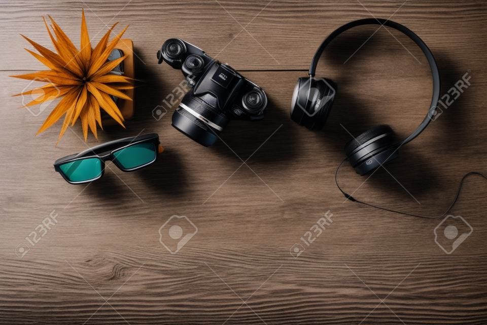 Bovenaanzicht van reisspullen. Camera, koptelefoon en glazen op houten tafel met kopieerruimte