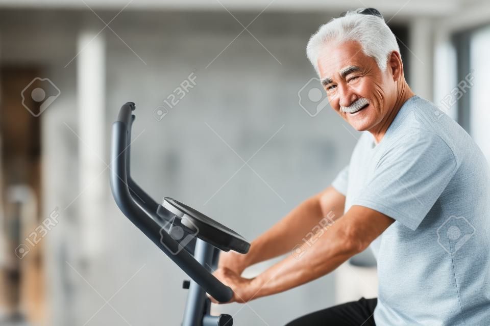 old senior man cycling, exercising, working out in gym with modern cycling machine