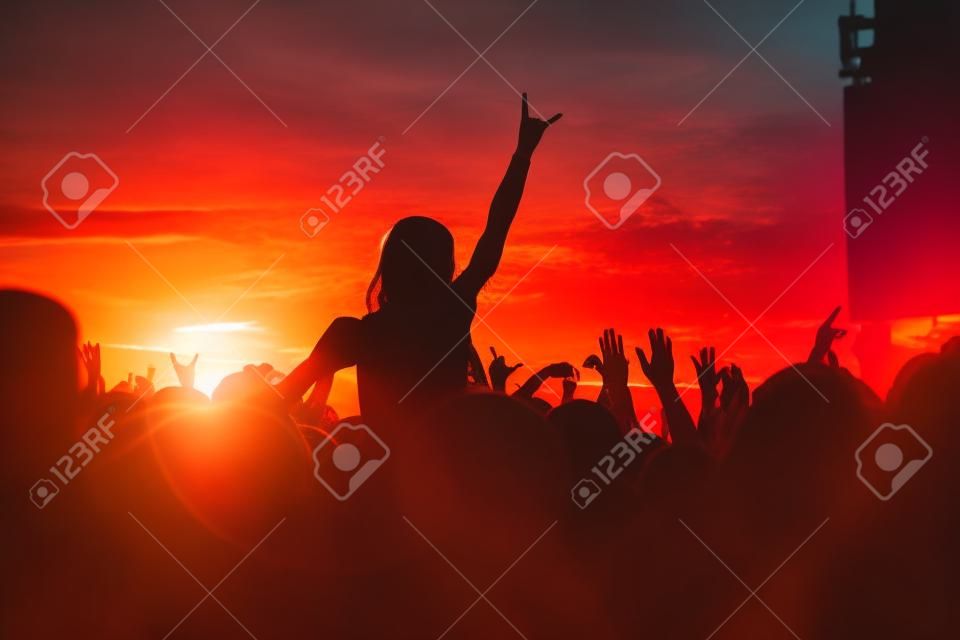 年轻的女孩喜欢一场摇滚音乐会，日落时的剪影，在露天举起手