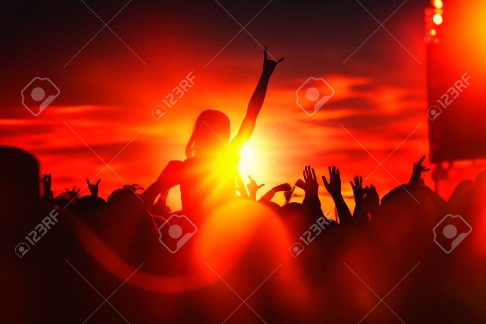 Young girl enjoys a rock concert, Silhouette on sunset, hands up on openair