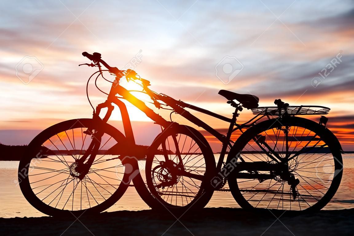 Black silhouette of a bicycle at sunset on the beach near the lake