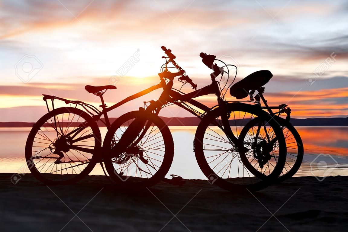 Siluetta nera di una bicicletta al tramonto sulla spiaggia vicino al lago