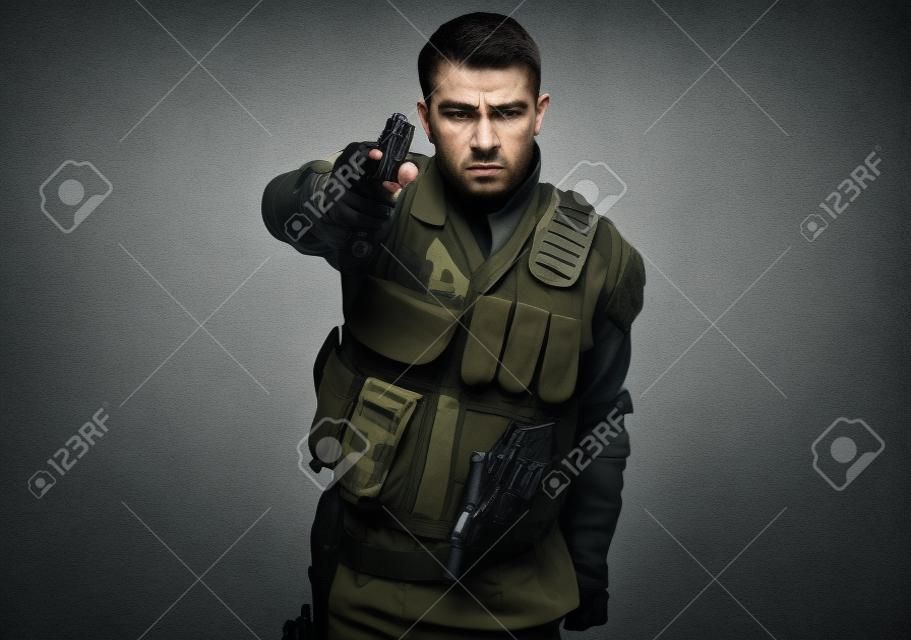 Retrato de soldado furioso con camuflaje urbano que apunta con la pistola sobre fondo gris