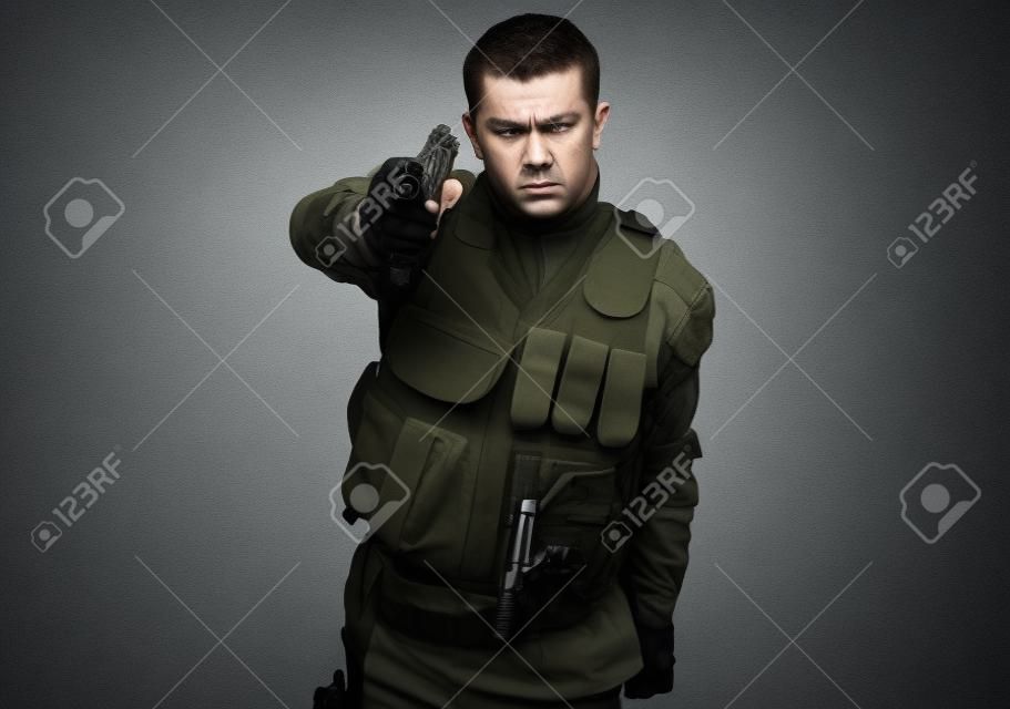 Retrato de soldado furioso con camuflaje urbano que apunta con la pistola sobre fondo gris
