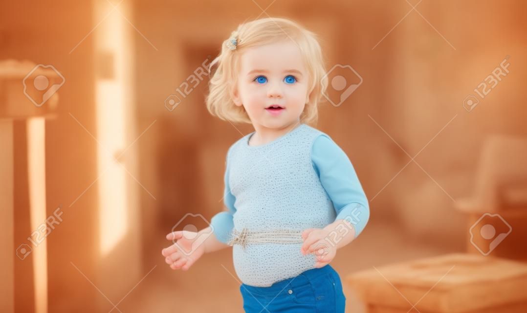 Bello bambino biondo con gli occhi azzurri che mostra l'ombelico in piedi a casa.