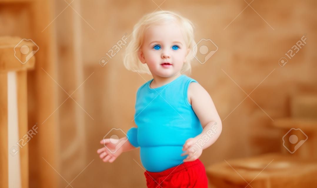 Bello bambino biondo con gli occhi azzurri che mostra l'ombelico in piedi a casa.