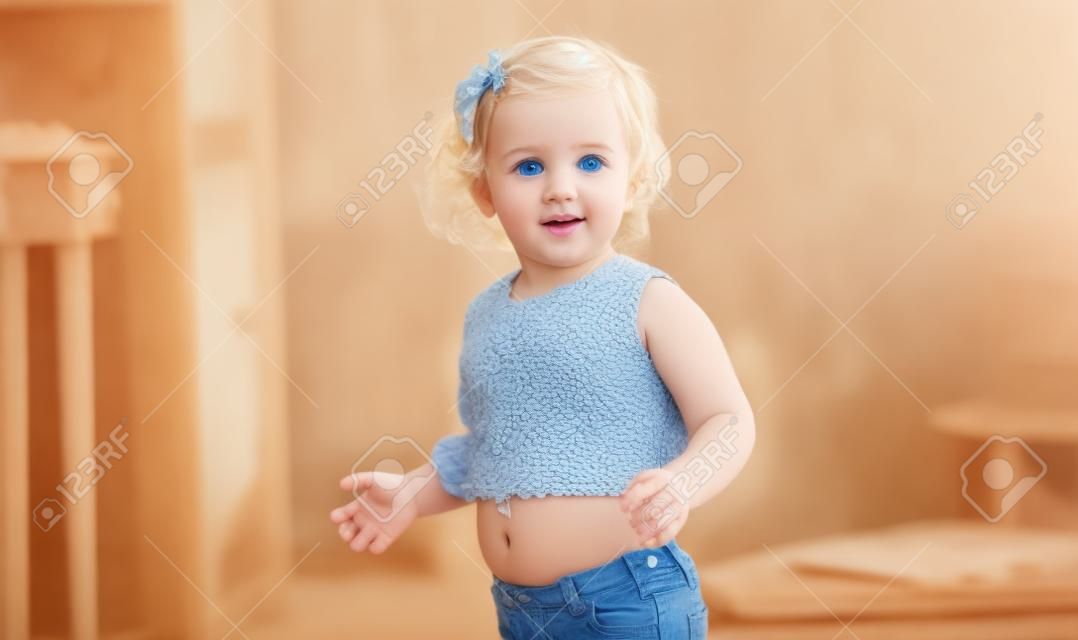 有站立的藍眼睛的美麗的白膚金發的孩子在家顯示肚臍。