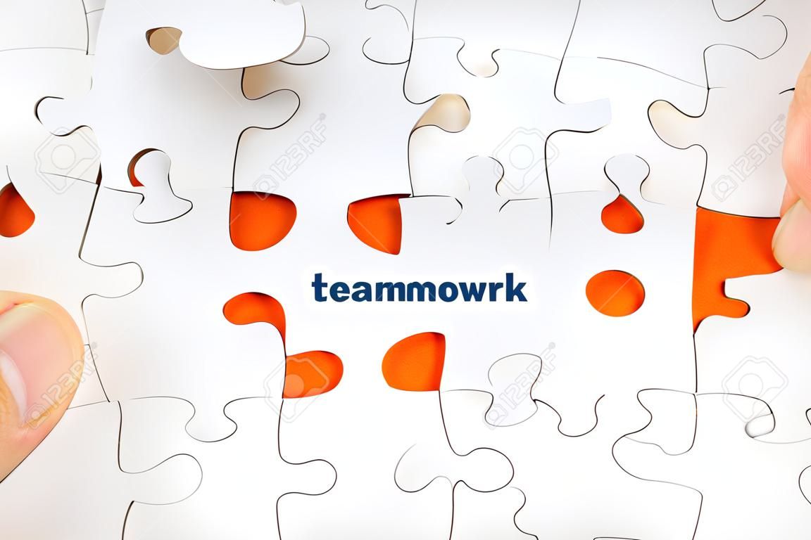 Hand holding piece of jigsaw puzzle with word TEAMWORK. Selective focus