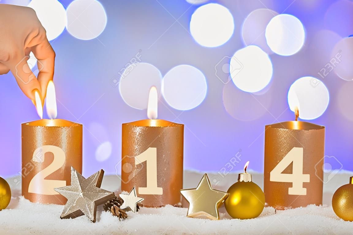 Four numbered gold advent candles with first candle lit by hand with match and christmas decoration lying in snow as template