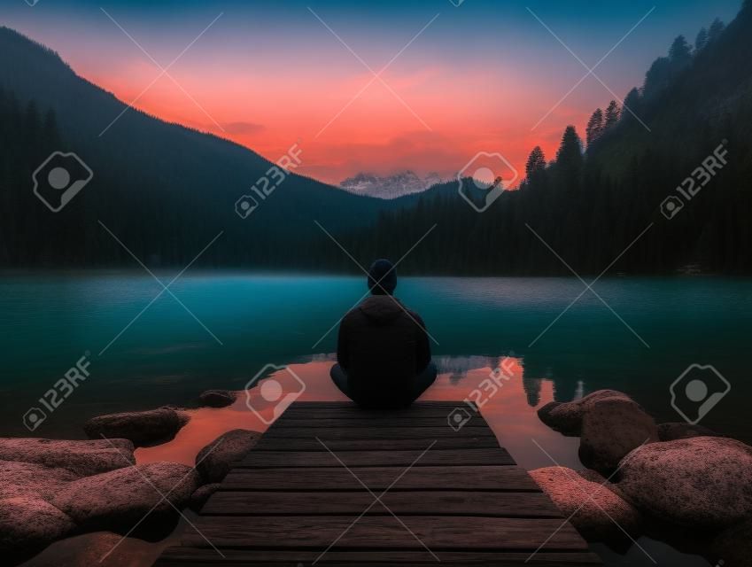a person sitting on a dock in front of a lake at dusk