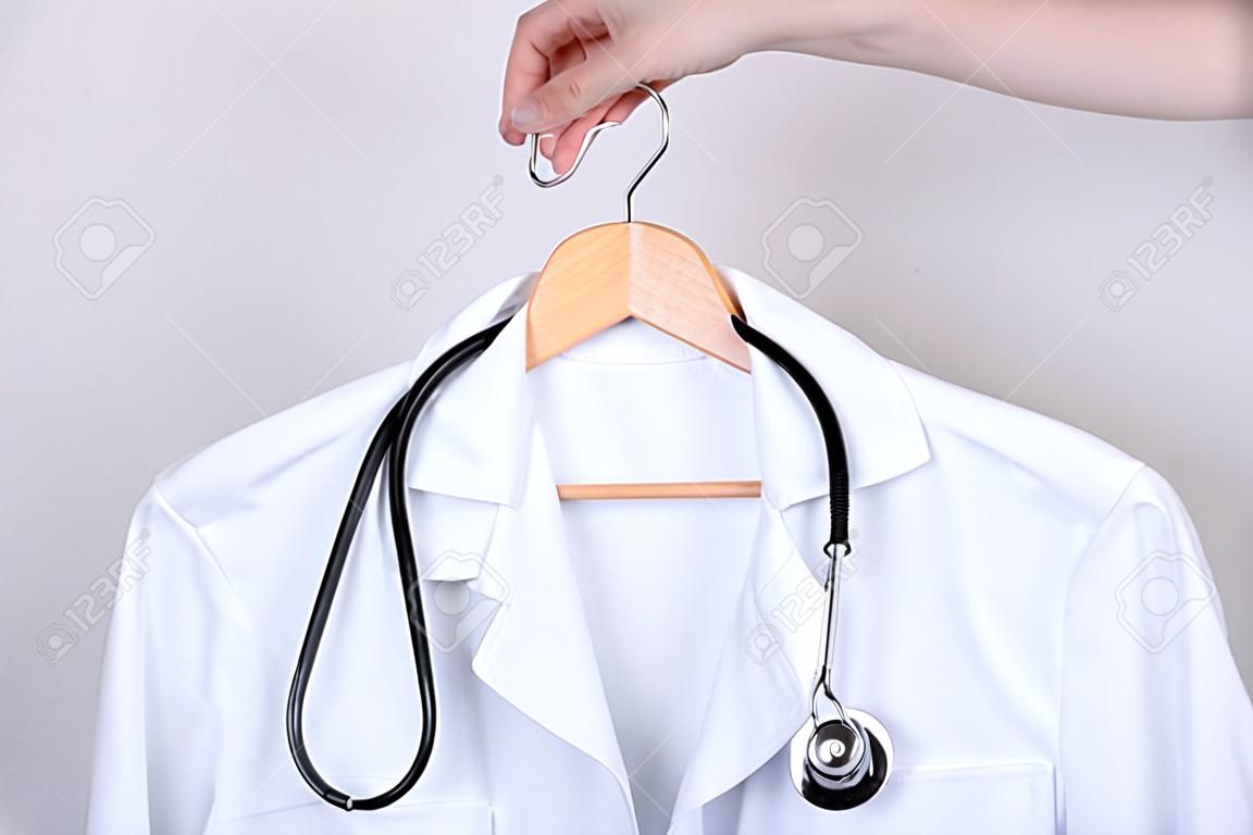 Job vacancy concept. Cropped close up photo of hand holding white doctor coat on hanger isolated over grey background