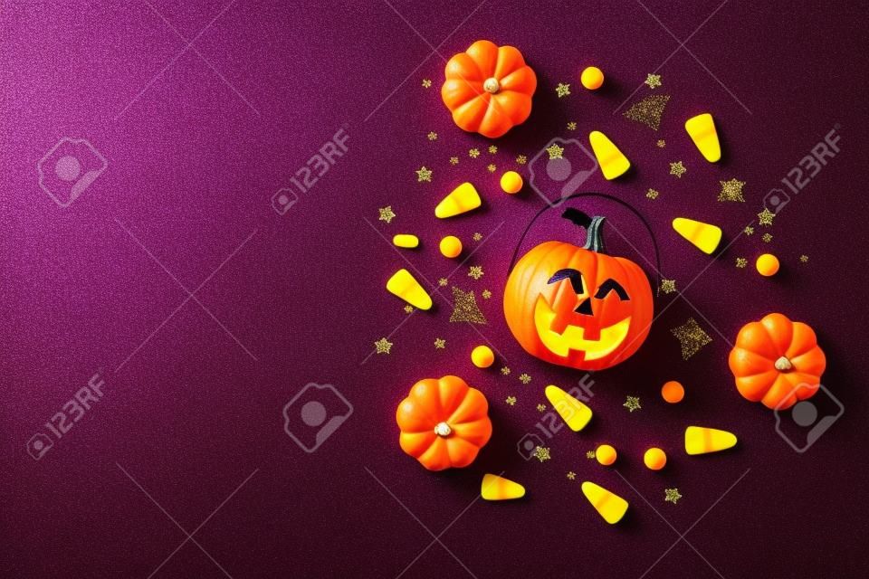 Vue de dessus photo de décorations d'halloween citrouilles panier bonbons maïs paillettes noires étoiles dorées chauve-souris toile d'araignée silhouettes sur fond violet isolé avec fond