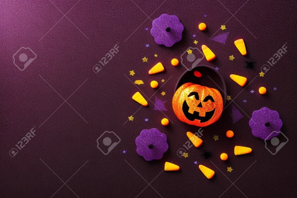 Top view photo of halloween decorations pumpkins basket candy corn black sequins golden stars bat spider web silhouettes on isolated violet background with copyspace