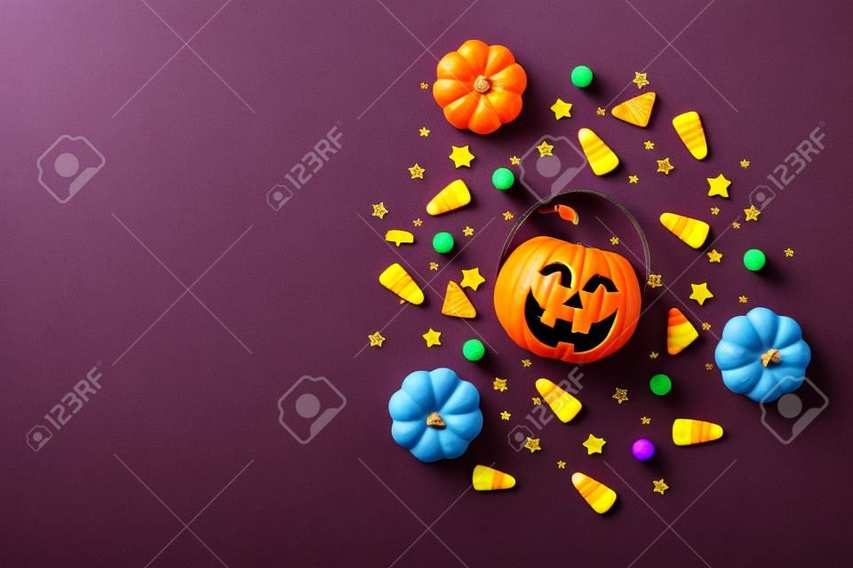 Top view photo of halloween decorations pumpkins basket candy corn black sequins golden stars bat spider web silhouettes on isolated violet background with copyspace