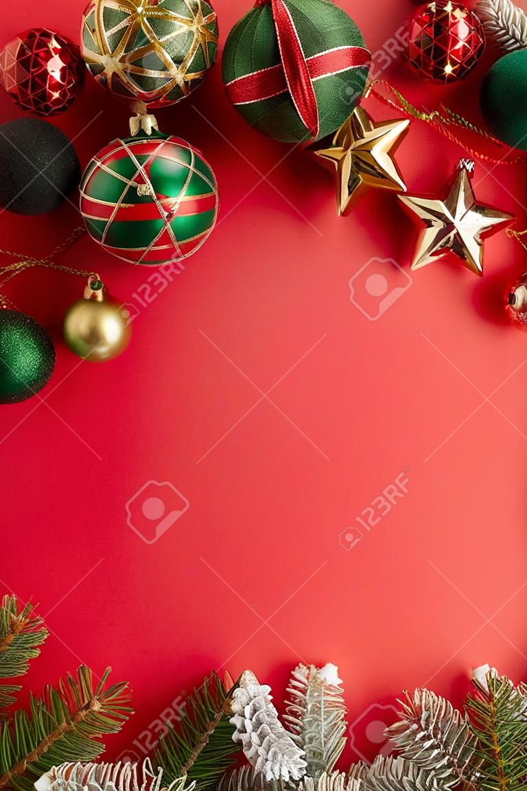 Christmas day concept. Top view vertical photo of pine branches in snow star ornaments gold green and red baubles on isolated red background with copyspace